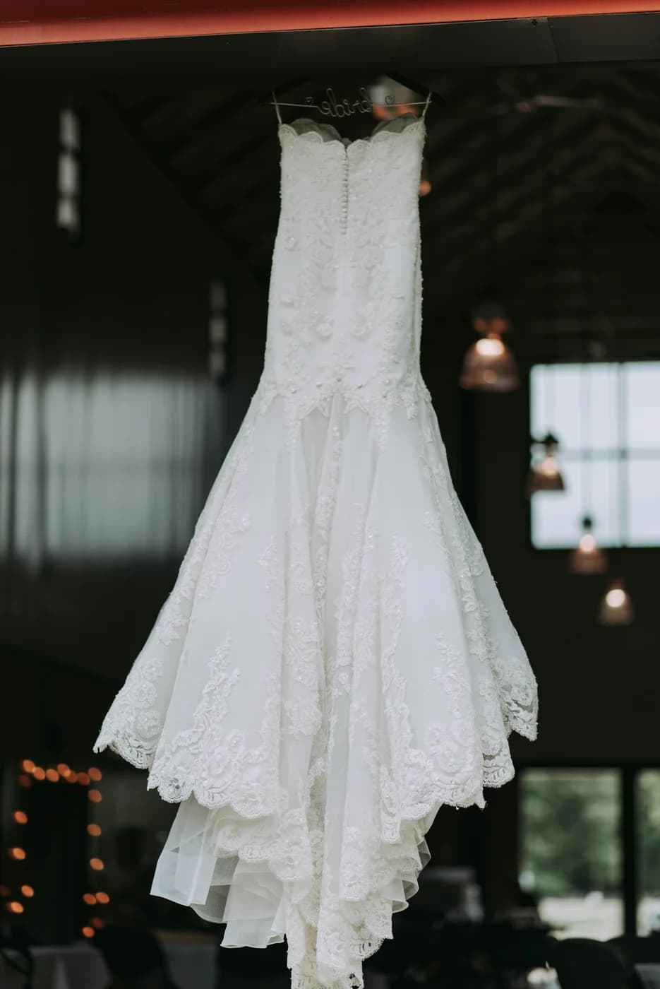 A white wedding gown hanging in a softly lit room at Atelier Bridal