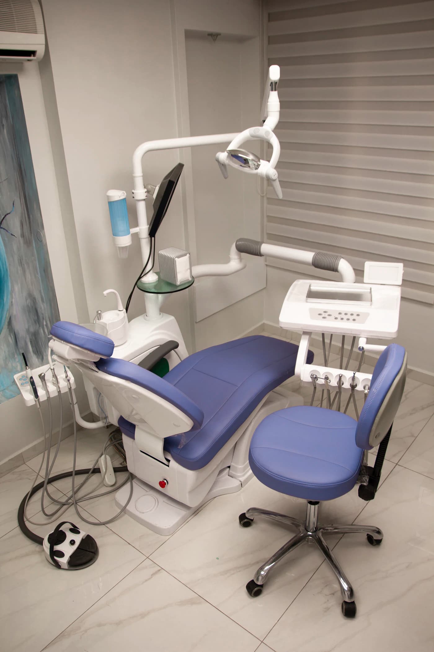 A dental treatment room with a blue chair and overhead light at Arc Smile Studio