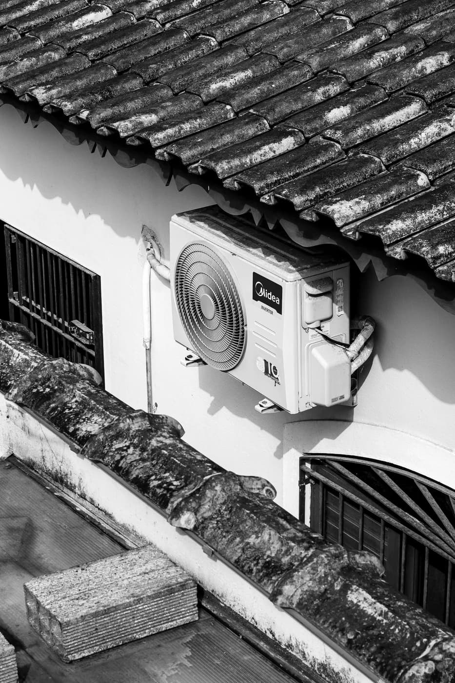 An outdoor air-conditioning unit mounted below a tiled roof at Comfort Air Systems