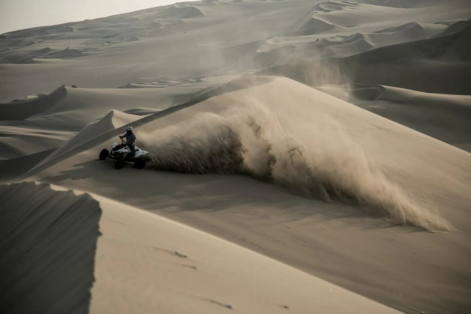 An ATV rider crossing a sweeping sand dune at Summit Powersports