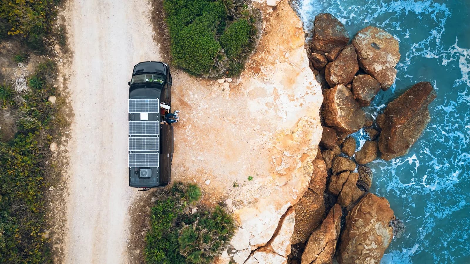 A campervan parked beside a rocky coast and turquoise water at Open Road RV
